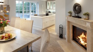 Une cuisine moderne avec une cheminée, un coin repas avec des chaises en osier et une grande fenêtre.