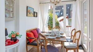 Et spiseområde med et bord dækket til fire personer, omgivet af træstole, en rød bakke og en vase med blomster.