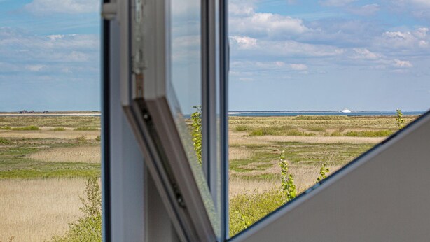 Udsigt fra et vindue over et fladt landskab med et fjerntliggende vand og en klar himmel.