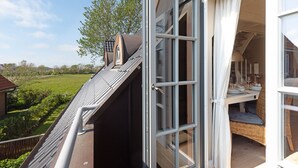 Janela aberta com vista para um jardim e uma área de jantar com mesa e cadeiras.