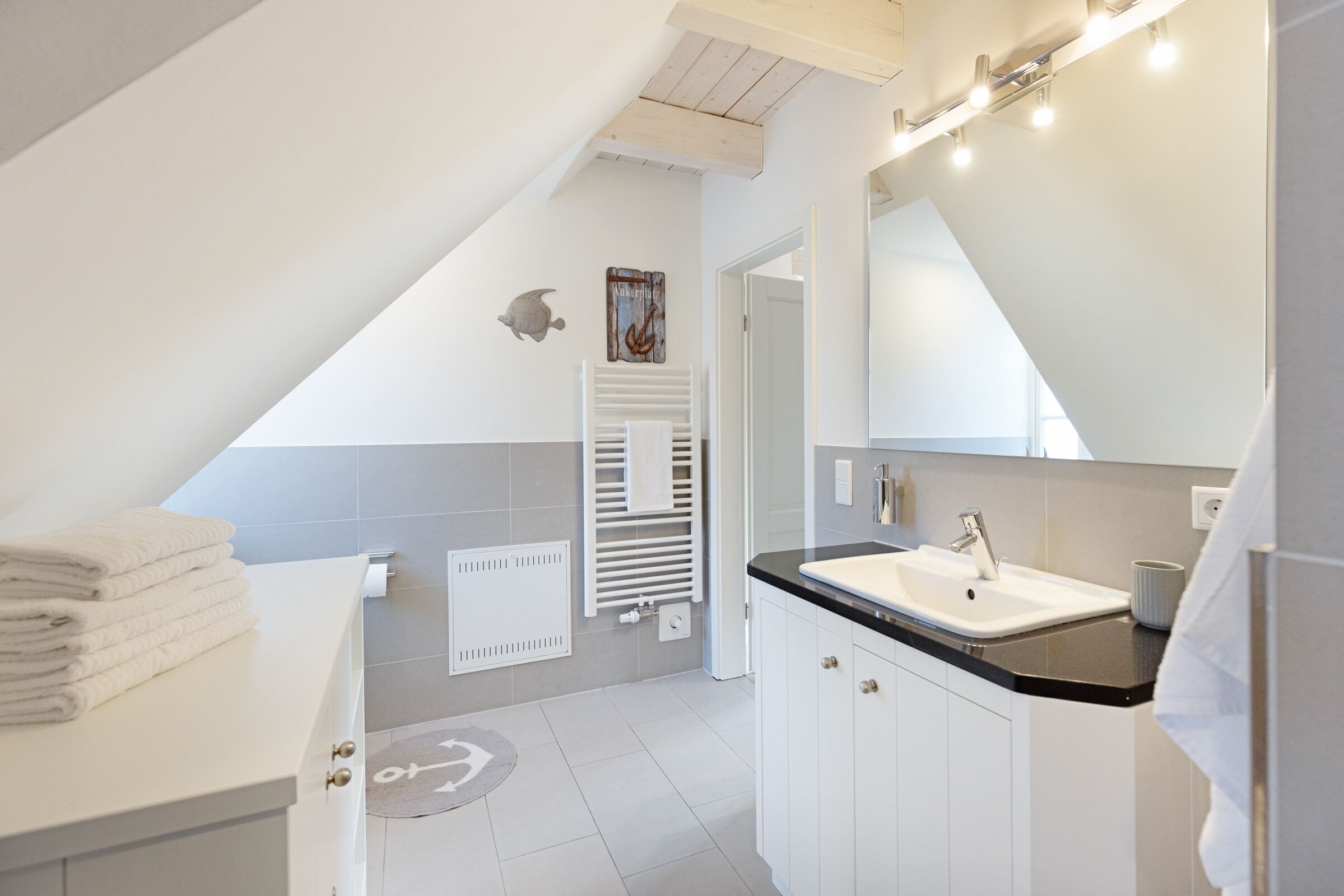 Un bagno moderno con un mobile lavabo bianco, un lavandino e uno specchio. Si nota uno porta asciugamani con asciugamani piegati e un termosifone a parete.