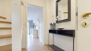 A hallway with a staircase, a console table with a vase of flowers, and a mirror on the wall.