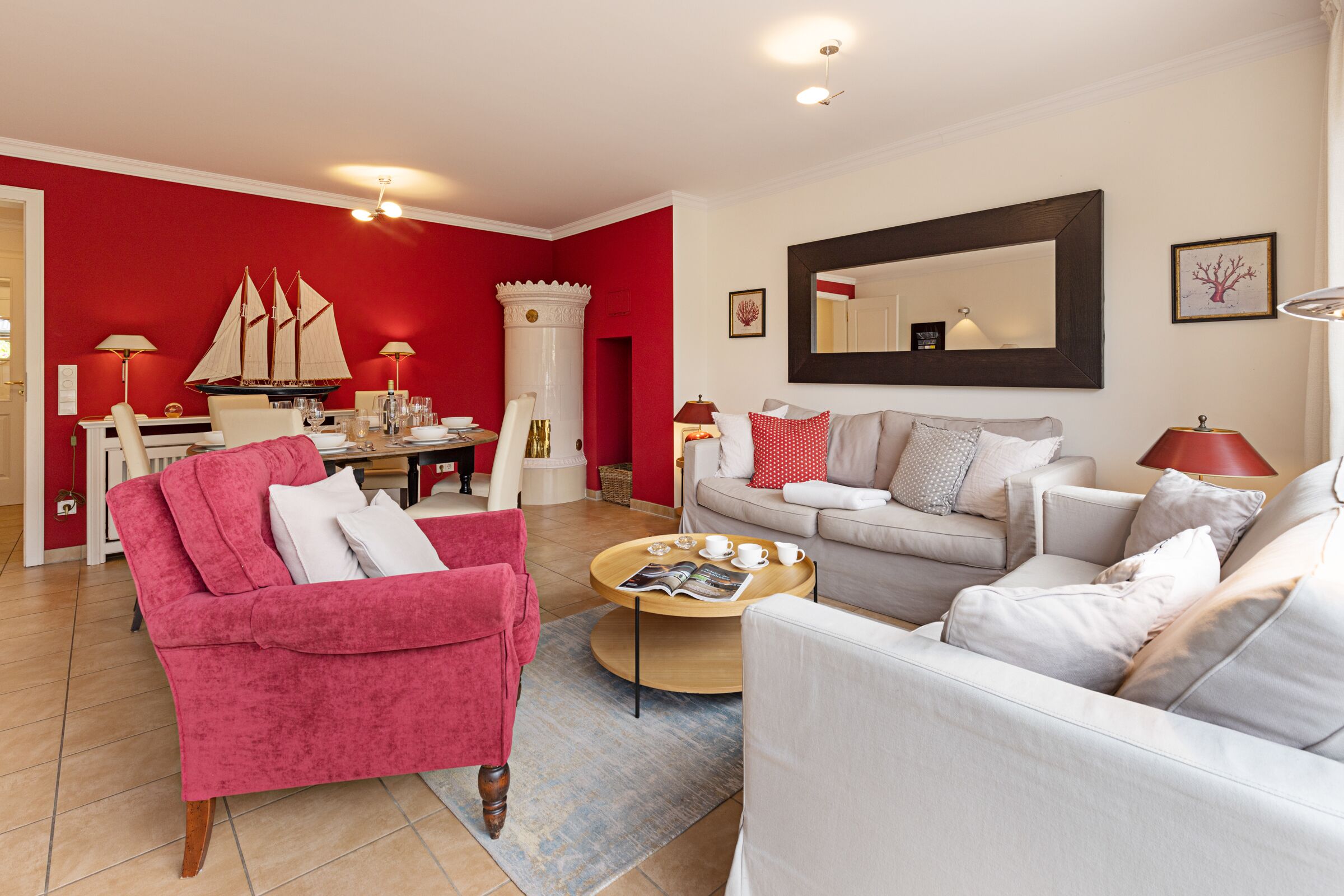A living room with a red accent wall, a white sofa, a pink armchair, and a wooden coffee table.