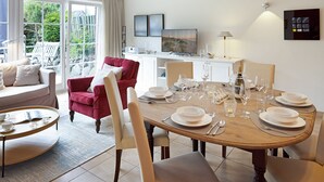 A dining area with a wooden table set for four, surrounded by chairs, and a red armchair. A television is mounted on the wall above the table.