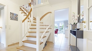 A modern interior with a wooden staircase, a kitchen area with a sink and countertop, and a view of the outdoors.