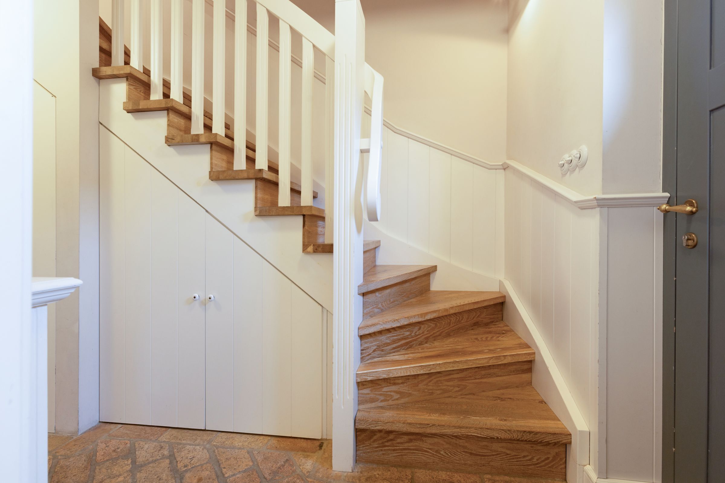 A staircase with wooden steps and white railings, leading to a door with a brass handle.