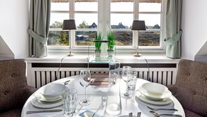 A dining table set for four with white plates, glasses, and cutlery, positioned in front of a window with a view of a landscape. - Herzlich Willkommen im Appartement Southend (List)