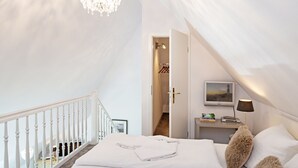 A bedroom with a white bed, fluffy pillows, a bedside table with a lamp, and a TV on the wall. - Herzlich Willkommen im Appartement Southend (List)