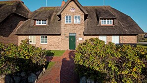 A traditional brick building with a thatched roof, a central entrance, and a small window with a ship symbol. - Herzlich Willkommen im Appartement Southend (List)