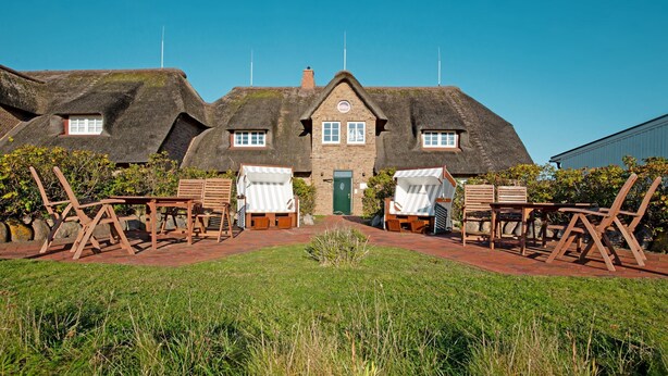 A traditional building with a thatched roof, a central entrance, and a paved area with wooden furniture. - Herzlich Willkommen im Appartement Southend (List)
