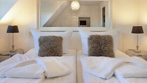 Ein Hotelzimmer mit zwei Betten, weißer Bettwäsche, flauschigen Kissen und einem großen Spiegel, der eine Treppe und einen Kronleuchter zeigt.