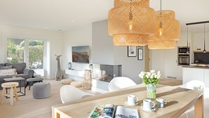 A modern living room with a wooden dining table, white chairs, and a large window. - Herzlich Willkommen im Ferienhaus Ellenbogenblick (List)