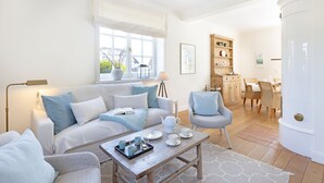 A living room with a sofa, armchairs, a coffee table, and a dining area with chairs and a table. - Welcome to the vacation home "Ferryview". (List)