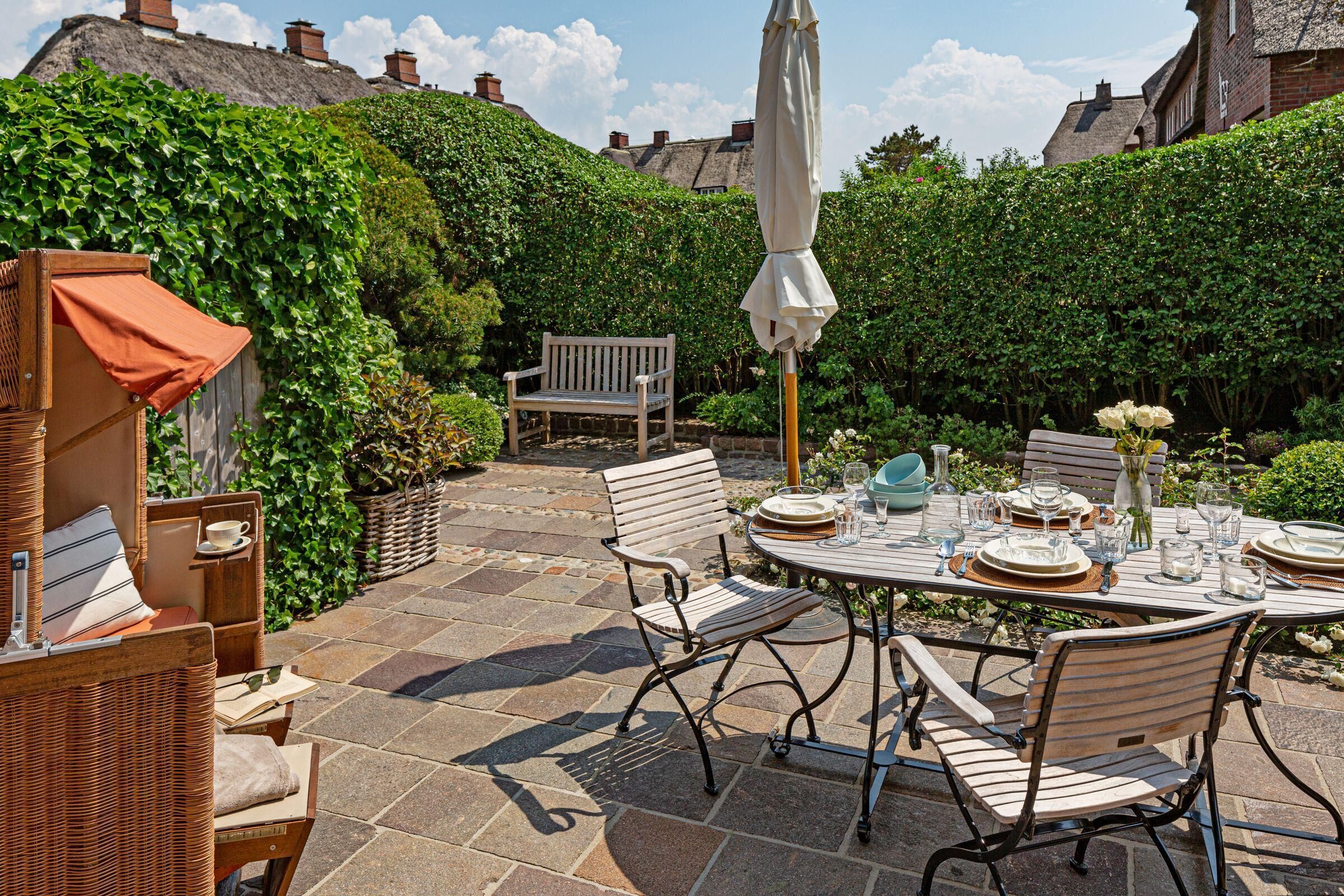 Eine Terrasse mit einem runden Esstisch, umgeben von Korbmöbeln und einer Bank.