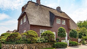 A traditional brick house with a thatched roof, stone wall, and well-maintained hedges. - Welcome to the vacation home "Ferryview". (List)