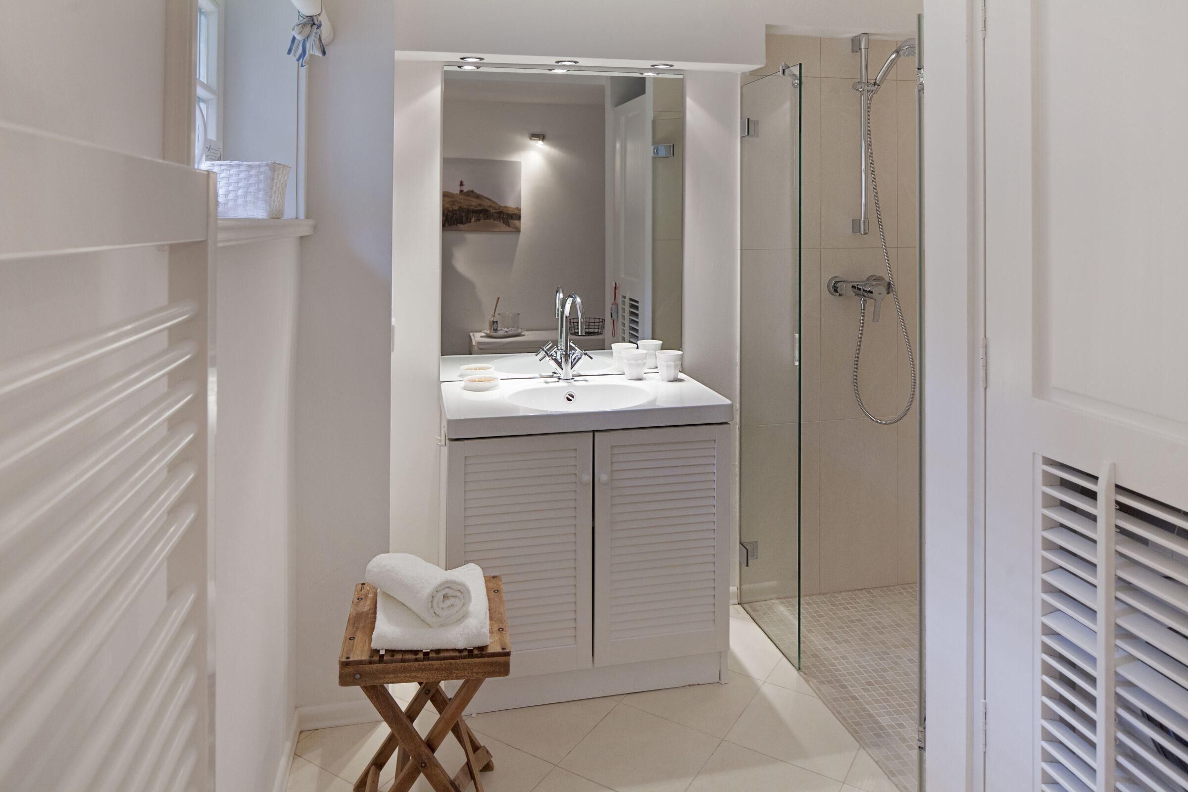 A modern bathroom with a large mirror, a white sink, and a glass-enclosed shower.