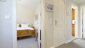 Un dormitorio con cama de madera, paredes blancas y una puerta que da a otra habitación.
