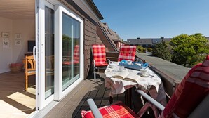 Un patio con una mesa lista para comer, sillas rojas de cuadros y una puerta corrediza de vidrio que da a una habitación.
