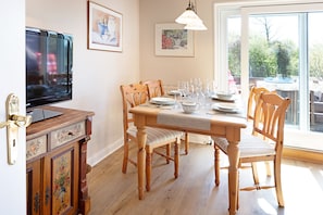 A dining area with a wooden table set for four, a television on the wall, and framed artwork on the walls.
