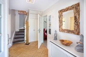A hallway with a staircase, a mirror, and a statue.