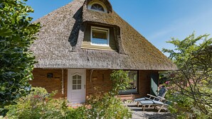 A thatched-roof cottage with a small window and a door, surrounded by greenery. - Herzlich Willkommen im Ferienhaus Fischers Koje (List)