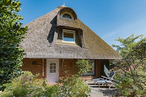 A thatched-roof cottage with a small window and a door, surrounded by greenery. - Herzlich Willkommen im Ferienhaus Fischers Koje (List)
