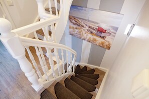 A staircase with white balusters and a wooden handrail, leading to a landing with a beach scene poster.