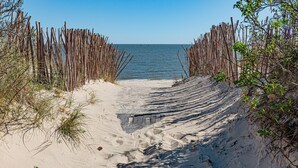 A sandy beach path leading to the sea, bordered by wooden fences and sparse vegetation.