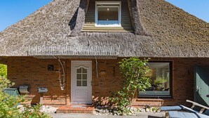 A thatched-roof cottage with a brick facade, a small porch, and a window with a view. - Herzlich Willkommen im Ferienhaus Fischers Koje (List)