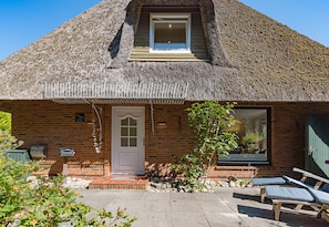 A thatched-roof cottage with a brick facade, a small porch, and a window with a view. - Herzlich Willkommen im Ferienhaus Fischers Koje (List)