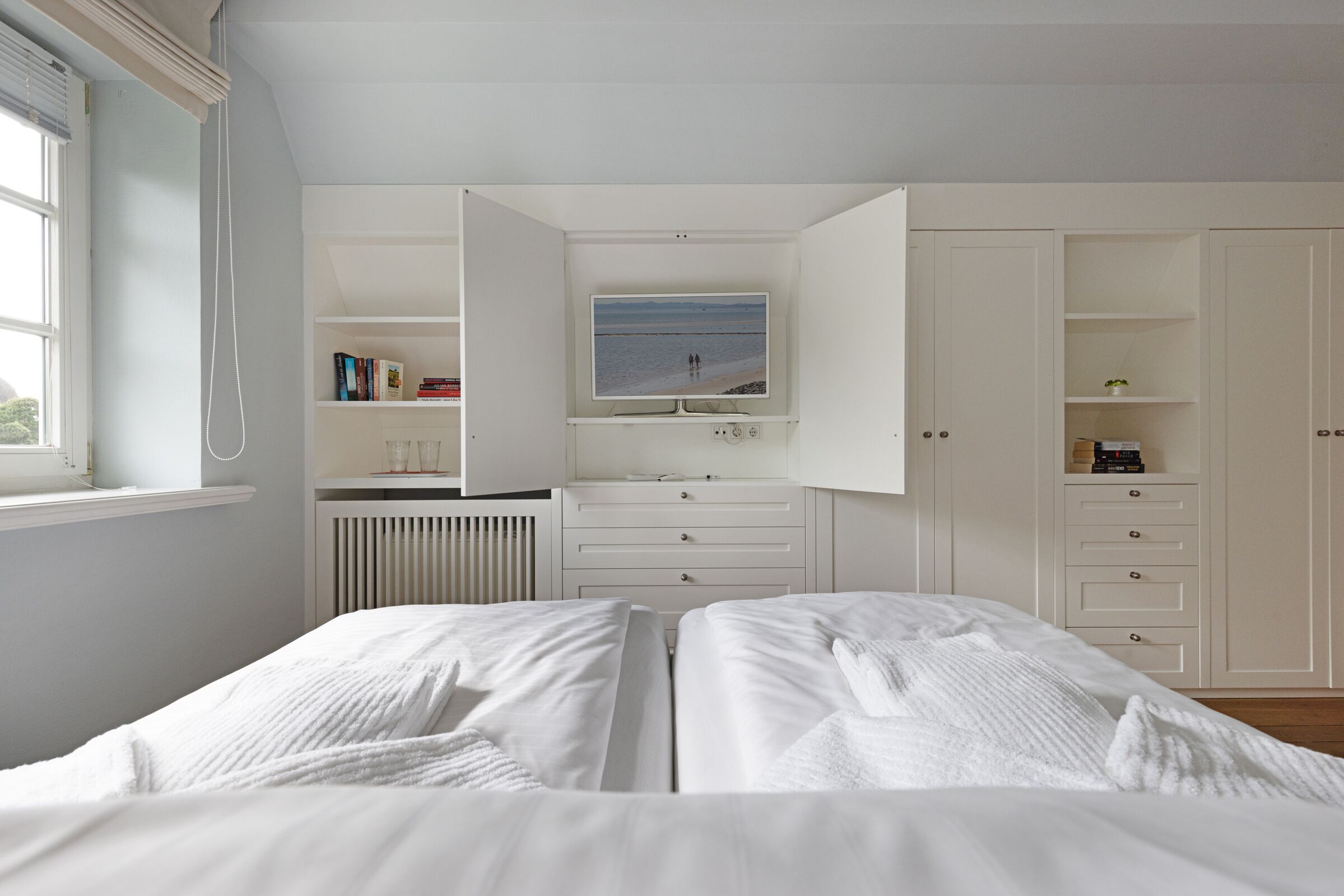 A bedroom with a bed, a TV, and a white wardrobe.