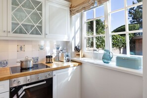 A kitchen with white cabinets, a stove, and a window with a view of greenery.