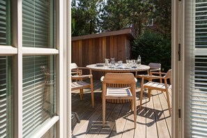 An outdoor wooden deck with a round table and six chairs, surrounded by a wooden fence.
