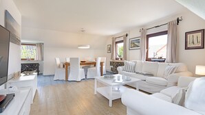 Un salón espacioso con un sofá blanco, una mesa de comedor con sillas y un televisor sobre un mueble.