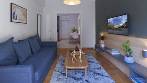 A modern living room with a blue sofa, a wooden coffee table, and a television mounted on the wall. - Marnis10 3rd (Athens)