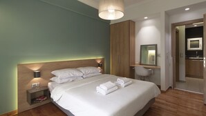 A modern hotel room with a large bed, bedside lamps, a desk with a chair, a mirror, and a wooden wardrobe. - Marnis10 3rd (Athens)