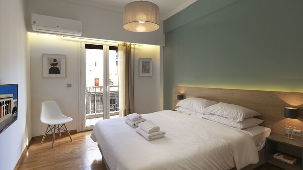 A modern bedroom with a large bed, a chair, a bedside table, and a view through a glass door. - Marnis10 3rd (Athens)