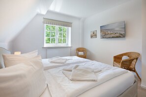 Ein Schlafzimmer mit zwei Betten, einem Fenster, einer Heizung, einem Sessel und einem Bild an der Wand.
