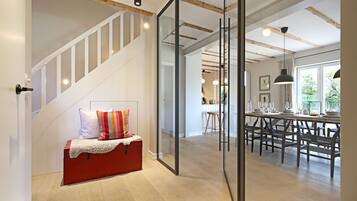 A modern interior with a staircase, a dining area with wooden furniture, and a kitchen in the background.