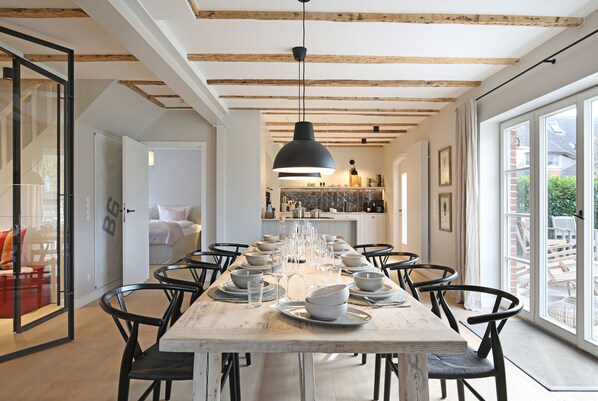 Enjoy a formal dining experience in this stylish space with a long table set for a meal, surrounded by comfortable chairs and a view of the outdoor patio.