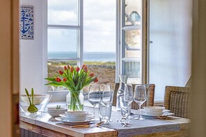 A dining table set with glassware and plates, a vase with red tulips, and a view of the sea through large windows. - Herzlich Willkommen im Appartement Lili (List)