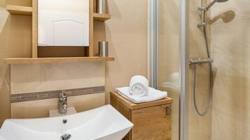 A bathroom with a white sink, wooden cabinet, and a glass shower enclosure.