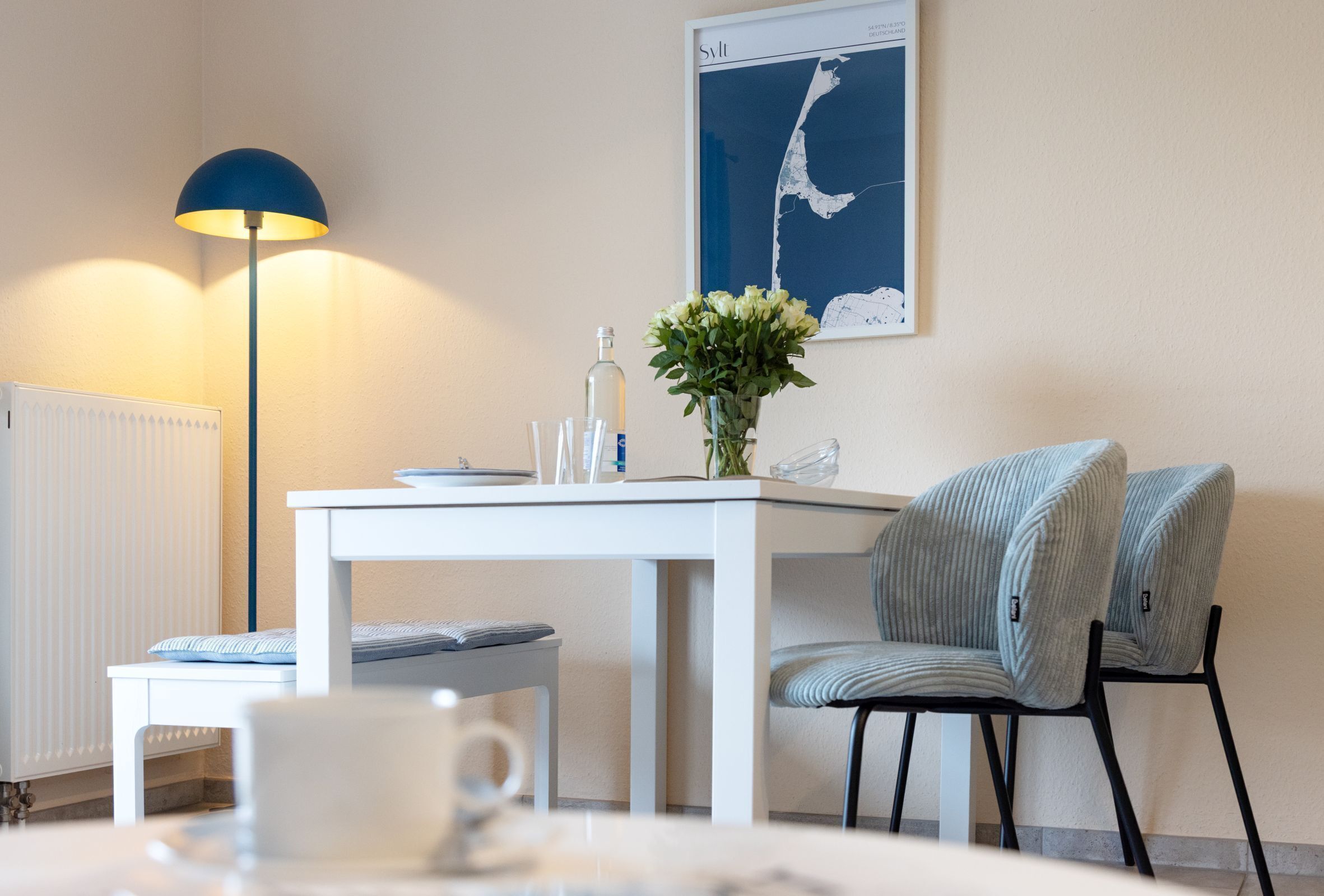 Ein modernes Zimmer mit einem weißen Tisch, einer blauen Lampe, einem Stuhl und einer gerahmten Karte an der Wand.