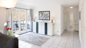 Ein modernes Wohnzimmer mit einer Couch, einem Couchtisch, einem Essbereich mit Stühlen, einer Küchenzeile und einem durch eine offene Tür einsehbaren Badezimmer.