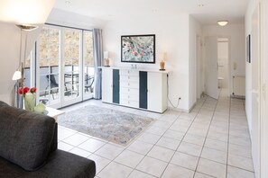 A modern living room with a sofa, a coffee table, a dining area with chairs, a kitchen area with a counter, and a bathroom visible through an open door.