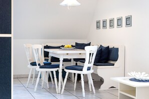 A dining area with a white table, four chairs, a bench with blue cushions, and a wall with framed pictures.