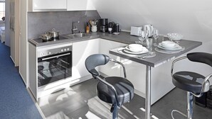 Una cocina moderna con horno empotrado, un lavamanos y una zona de comedor con dos taburetes de bar y una mesa preparada para dos personas.