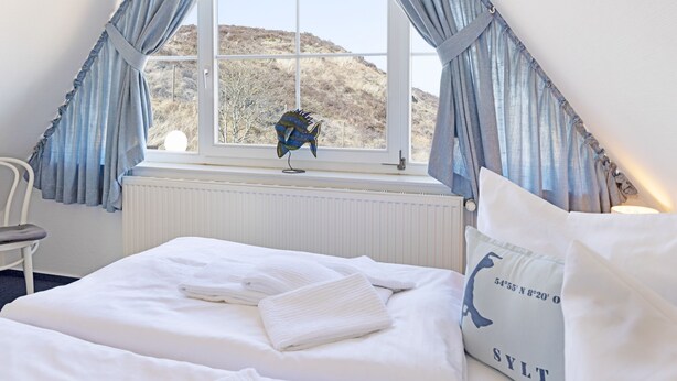Un dormitorio con una cama, una ventana con cortinas, un radiador y un adorno de pez colgando cerca de la ventana.