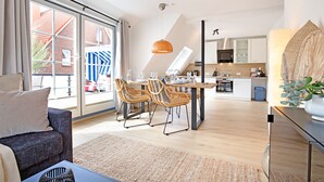 Ein modernes Wohnzimmer mit einer Couch, einem Esstisch mit Stühlen und einer Küche im Hintergrund.