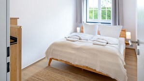 Ein Schlafzimmer mit einem Bett, einem Fenster, einem Nachttisch und einem Holzschrank.
